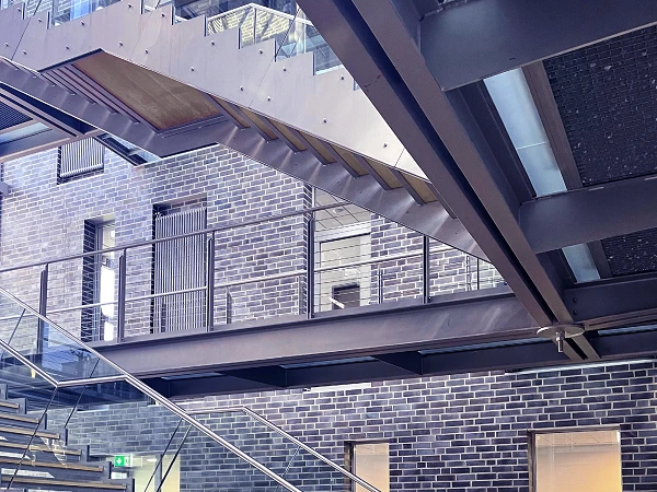 Eine moderne Innenarchitektur zeigt eine Treppe aus Metall und Holz, die über eine helle, offene Fläche in einem Raum mit Backsteinwänden führt.