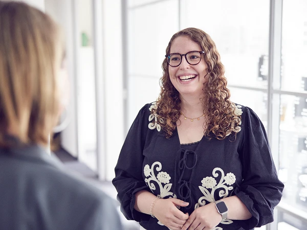 Junge Frau mit Brille lächelt während eines Gesprächs im Büroflur