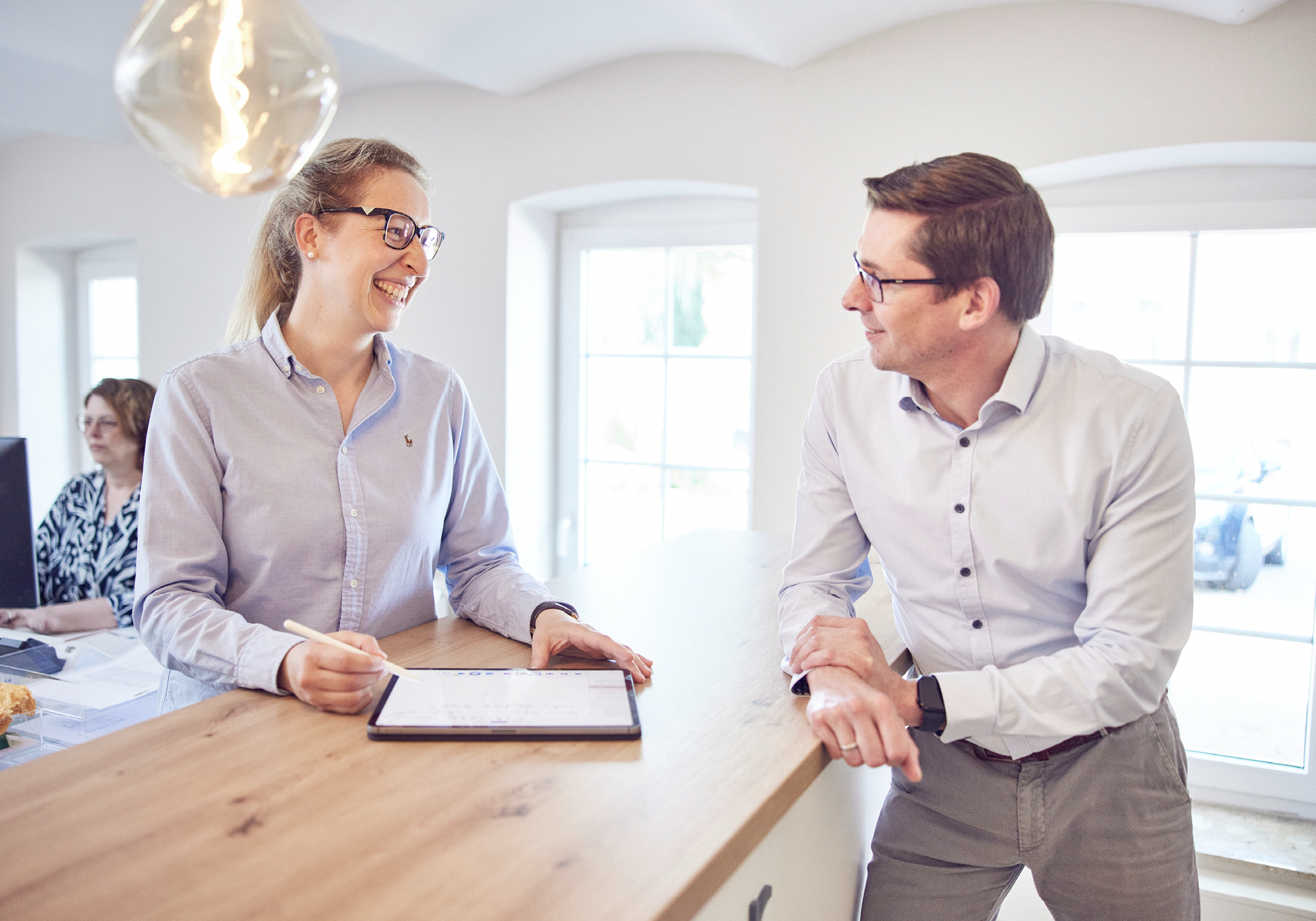 Zwei Kolleg:innen im Gespräch an einem Stehtisch mit Tablet
